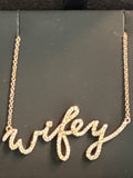 A gold script name necklace spelling 'wifey' with small clear stones, displayed on a black jewelry card.
