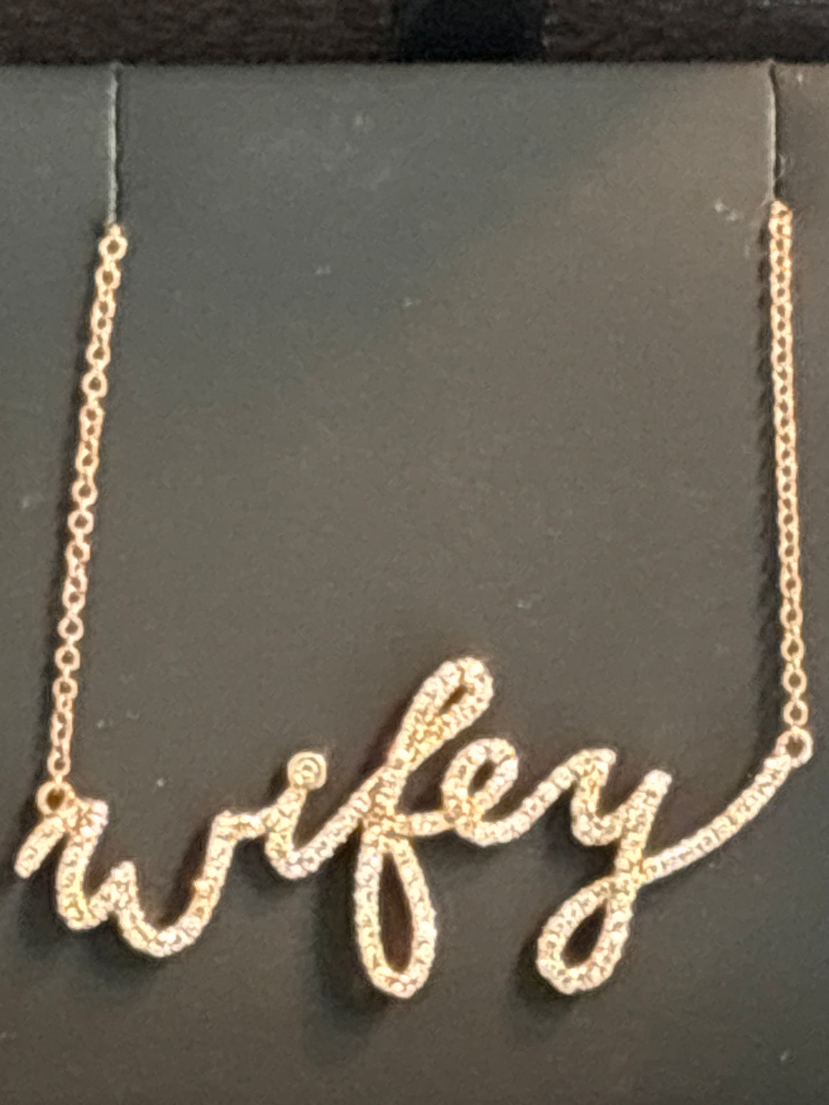 A gold script name necklace spelling 'wifey' with small clear stones, displayed on a black jewelry card.